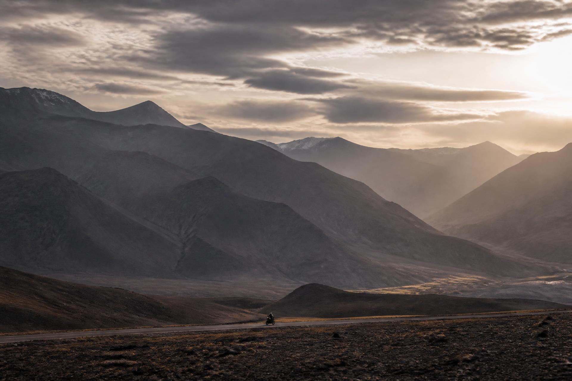 A lone motorcycle crossing an enormous mountain landscape at dawn